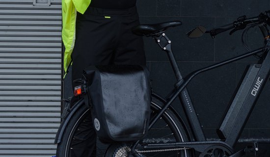 Zwarte AGU regenbroek gedragen door een man naast een fiets met een zwarte fietstas.