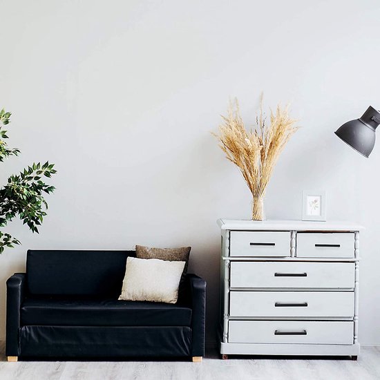 Zwarte tweezitsbank met kussens, naast een witte commode met bruine droge bloemen.