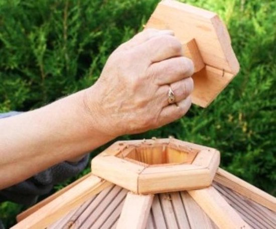 Hand met ring verwijdert achthoekige houten deksel van vogelhuisje.