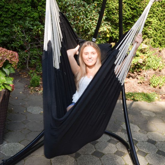 Lachende vrouw met blond haar ontspant in een zwarte hangstoel met witte touwen, buiten.