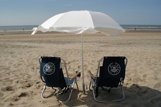 Twee donkerblauwe campingstoelen onder een witte parasol op een zonnig strand.