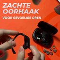 Hand houdt een zwart sport oordopje vast, met oplaadcase en eartips op de achtergrond.