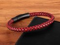 Rood gevlochten leren armband met matzwarte RVS kliksluiting, rustend op een zwart notitieboekje.
