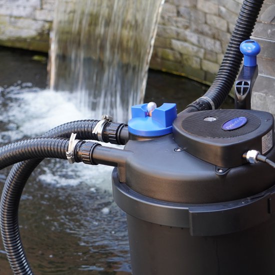 Zwarte vijverfilter met blauwe dop en handgreep, naast een waterval.