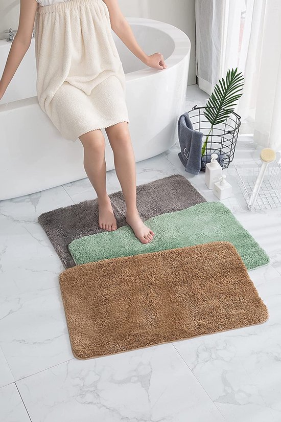 Drie badmatjes in beige, groen en grijs op een badkamervloer.