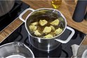 Een RVS pan met tortellini in bouillon op een inductiekookplaat. Een kleinere RVS pan staat ernaast.