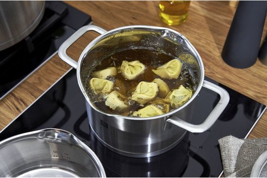 Een RVS pan met tortellini in bouillon op een inductiekookplaat. Een kleinere RVS pan staat ernaast.