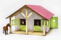 Houten paardenstal met roze dak, groene luiken en deuren. Twee paardenkoppen kijken uit de boxen.