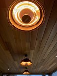 Twee zwarte hangende terrasverwarmers met gloeiende spiraal aan een houten plafond.