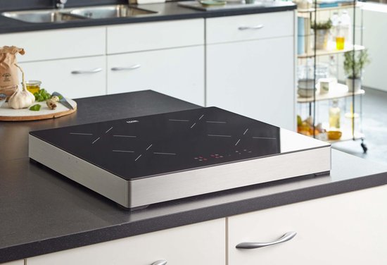 Une plaque de cuisson à induction carrée autoportante avec une surface en verre noir et un cadre en métal brossé, placée sur un plan de travail.