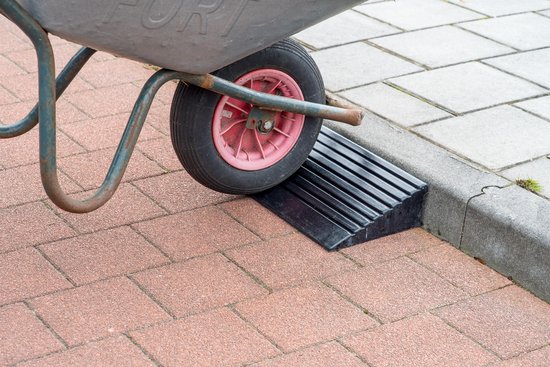 Zwarte, geribbelde drempelhulp voor een stoeprand, met een kruiwiel erop.
