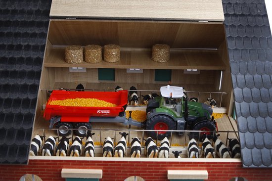 Speelgoedboerderij met in de stal zwart-wit koeien, een rode aanhanger met mais en een groene tractor.