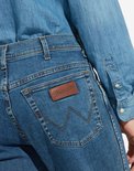 Close-up van de achterkant van een blauwe Wrangler spijkerbroek met bruin leren logo op de zak.