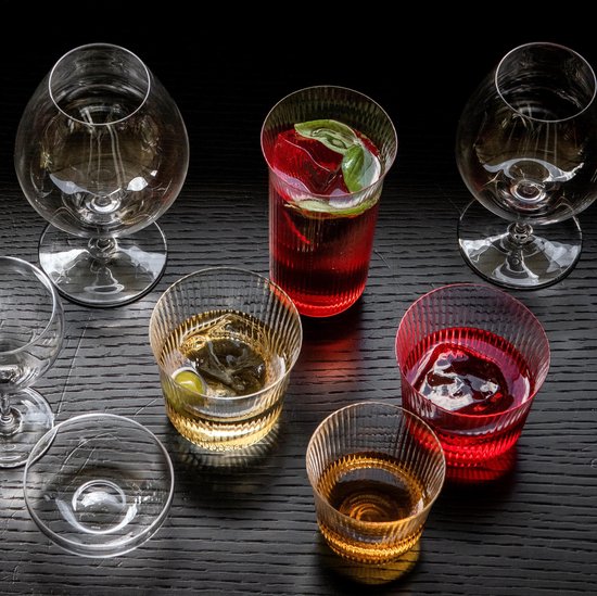Verschillende glazen met drankjes op een donkere, houten tafel, waaronder geribbelde glazen.