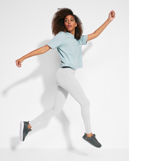 Vrouw in de lucht met een lichtblauwe top en grijze legging, sneakers.
