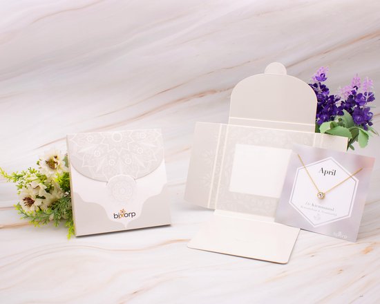 Een gouden ketting met zirkonia hanger op de 'April' kaart, naast een open geschenkdoos.
