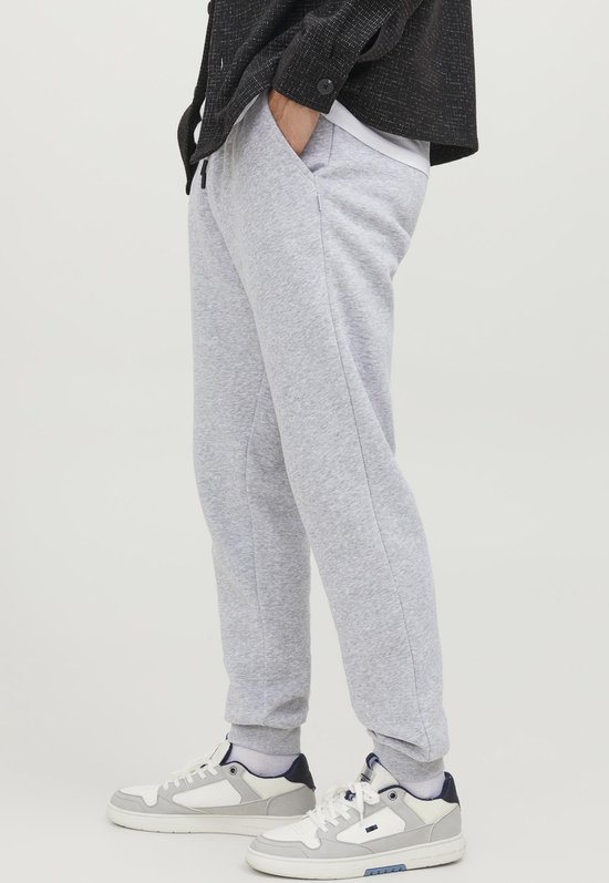 Man met lichtgrijze joggingbroek en witte sneakers, gedragen met een donkere jas.