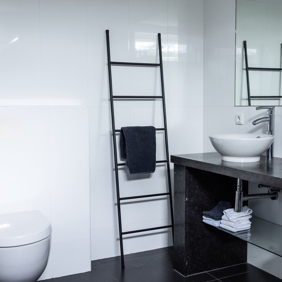 Zwarte decoratieve ladder in een badkamer, met een donkergrijze handdoek erop.