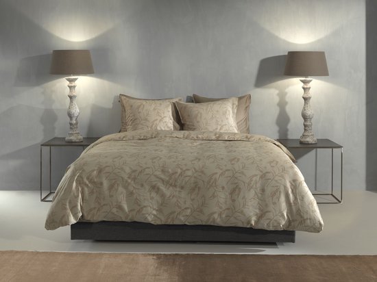 Opgemaakt bed met beige dekbedovertrek met bladermotief, omringd door decoratie.
