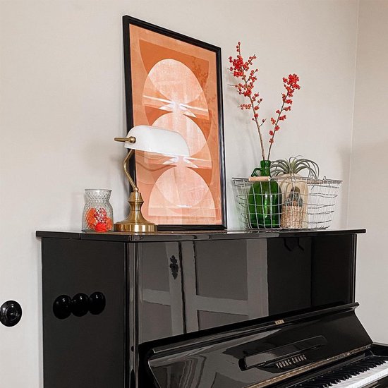 Lampe de bureau dorée sur un piano noir, à côté d'une grande bouteille verte avec des baies rouges.