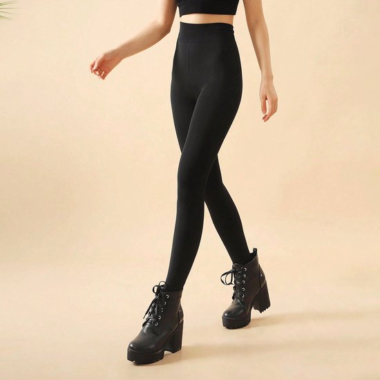 Een model draagt een zwarte, nauwsluitende legging met hoge taille en zwarte plateau laarzen met veters.