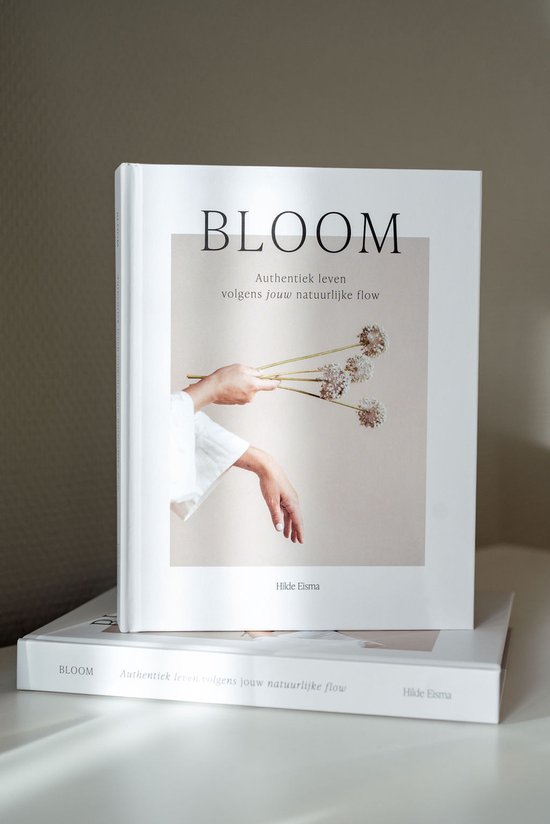 Boek 'BLOOM Authentiek leven volgens jouw natuurlijke flow' met hand die bloemen vasthoudt.
