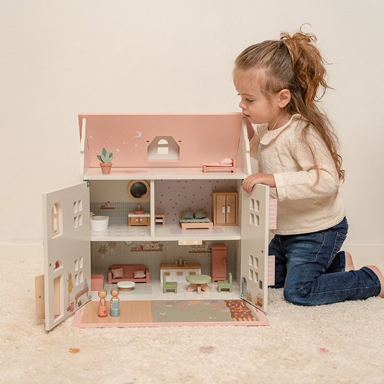 Meisje speelt met een houten poppenhuis met roze dak, openklapbare deuren en gedetailleerde kamers.