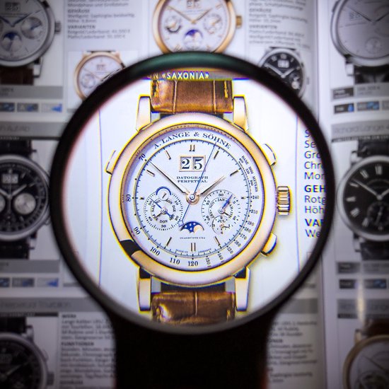 Gouden horloge met bruin lederen band, vergroot in een catalogus, met datum en maanfase.