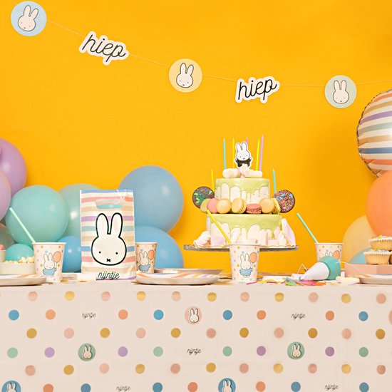 Gâteau à deux étages avec glaçage crème, macarons et bougies, entouré de décorations festives.