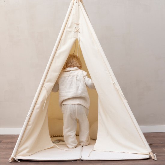 Een jong kind in een crèmekleurig pak loopt een tipi tent in. De tent is open en heeft touwen aan de zijkant.