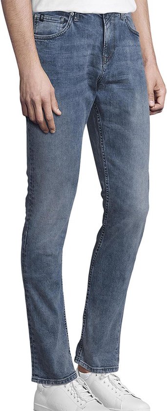 Man met lage taille, staand in een blauwe denim jeans, witte sneakers.