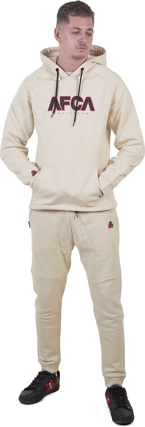 Man in crème joggingbroek en hoodie met AFCA AMSTERDAM-logo. De broek heeft een logo op de heup.