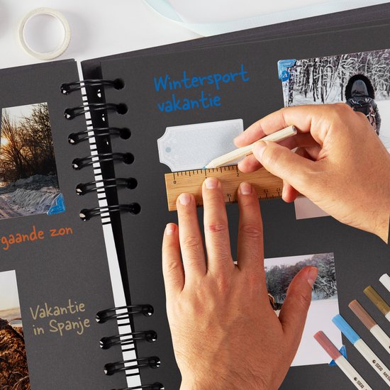 Handen met een liniaal en potlood op een zwart plakboek. De tekst 'Wintersport vakantie' is geschreven.