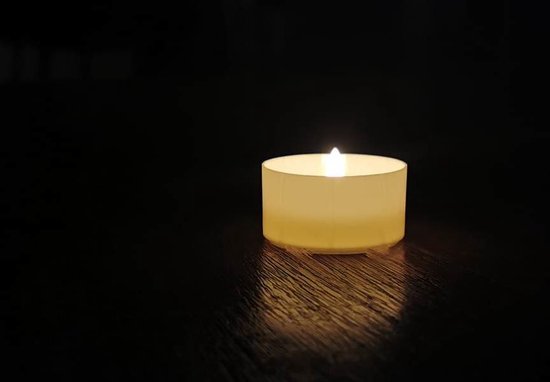 Eén brandend C-lights theelichtje op een donkere houten ondergrond.