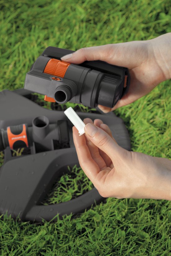 Des mains assemblent un arroseur GARDENA sur une base.
