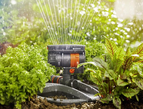 Arroseur oscillant GARDENA compact dans un jardin verdoyant avec des jets d'eau.
