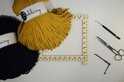 Okergele en zwarte Bobbiny macramé garenbundels naast een macramé weefgetouw.