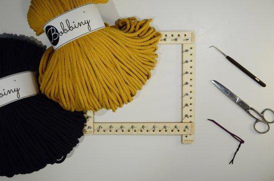 Okergele en zwarte Bobbiny macramé garenbundels naast een macramé weefgetouw.