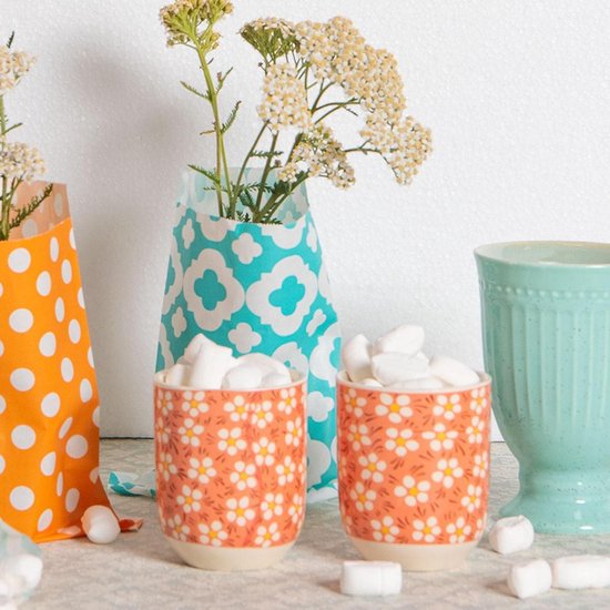 Twee oranje mokken met bloemenprint, gevuld met marshmallows, naast oranje en blauwe vazen met bloemen.