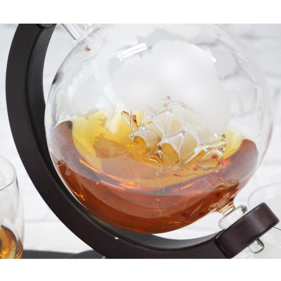 Close-up van glazen wereldbol karaf met amberkleurige drank en schip, op houten standaard.