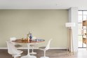 Lichte groene muur in een eetkamer met ronde tafel, stoelen, en een staande lamp.