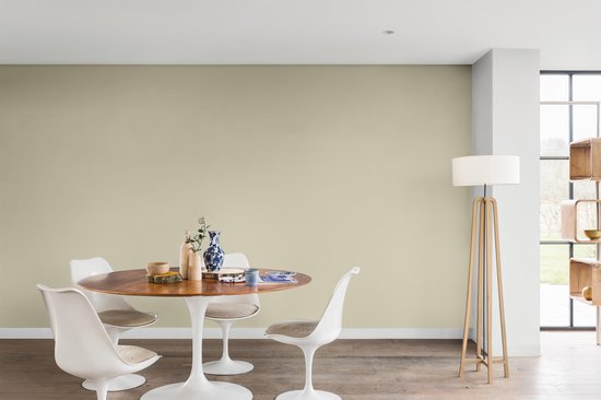 Lichte groene muur in een eetkamer met ronde tafel, stoelen, en een staande lamp.