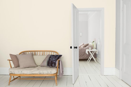 Houten bankje met kussens in een lichte kamer met open deur naar slaapkamer.