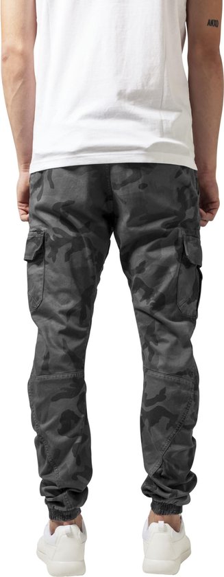 Man met camouflage cargo broek, wit T-shirt en witte sneakers, van achteren gezien.
