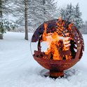 Roestbruine vuurschaal in bolvorm met open gesneden dieren en bomen, brandend in de sneeuw.