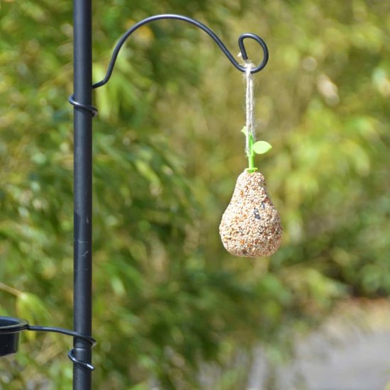 Peer-vormig vogelvoer, bedekt met zaden, hangt aan een haak van een zwart vogelvoederstation.