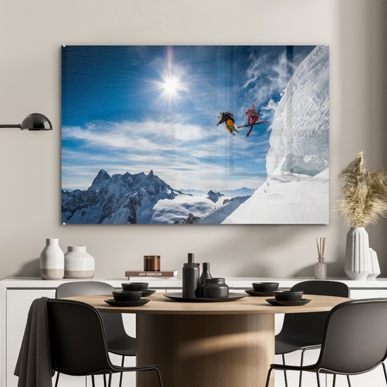 Glasschilderij met skiërs die springen, hangend boven een eettafel.