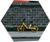 PVC Schuimplaat Hexagon - Gele Fiets Geparkeerd tegen Stenen Muur - 50x43.5 cm Foto op Hexagon (Met Ophangsysteem)