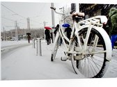 PVC Schuimplaat- Fiets Geparkeerd in Stad tijdens Sneeuwbui - 105x70 cm Foto op PVC Schuimplaat