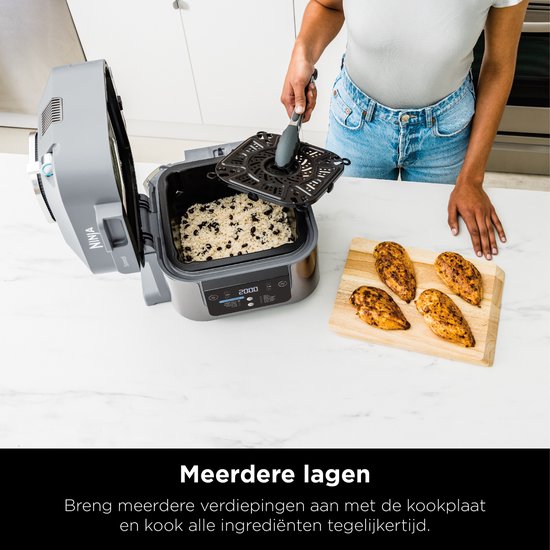 Vrouw met spijkerbroek gebruikt Ninja Speedi met open deksel, met rijst en kip erin. Kookplaat voor meerdere lagen.